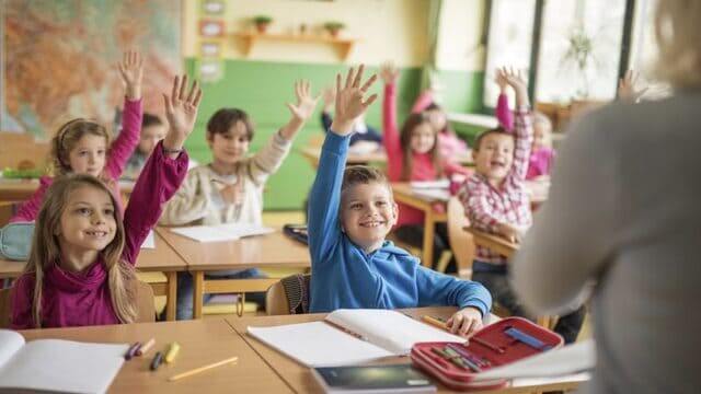 أطفال يجلسون في فصل مدرسي ويرفعون أيديهم للإجابة والتفاعل مع المدرسة
