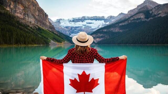 فتاة تقف وتحمل علم دولة كندا أمام مسطح مائي وجبال